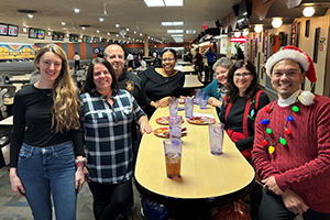 Photo of President Moore and staff gathering around a table in a bowling alley