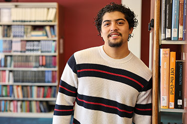 Photo of Emiliano Medellin standing in front of Shelves with books